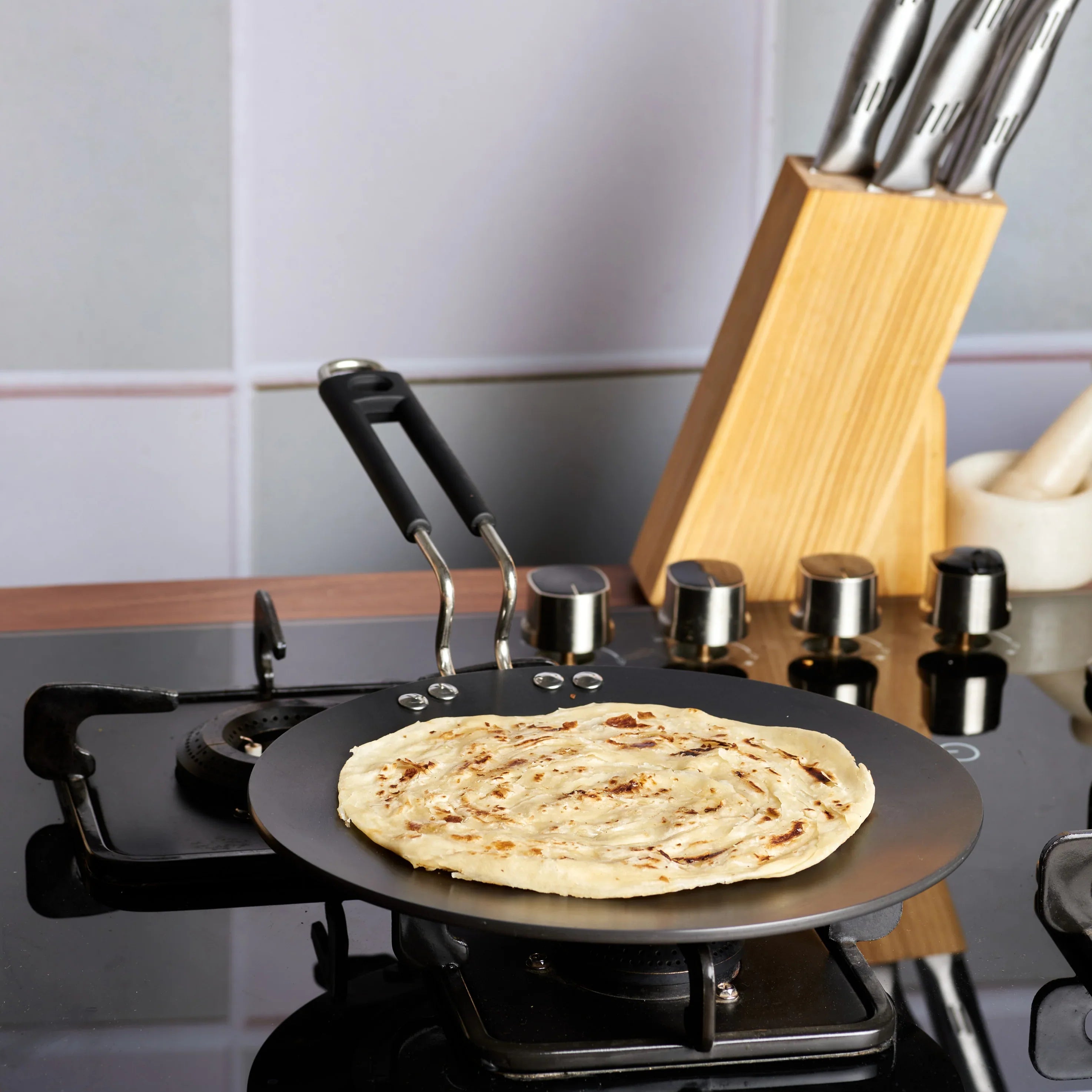 Perfect layered paratha being cooked on Vinod Hard Anodised Flat Tawa on gas stove showing excellent even heat distribution and browning